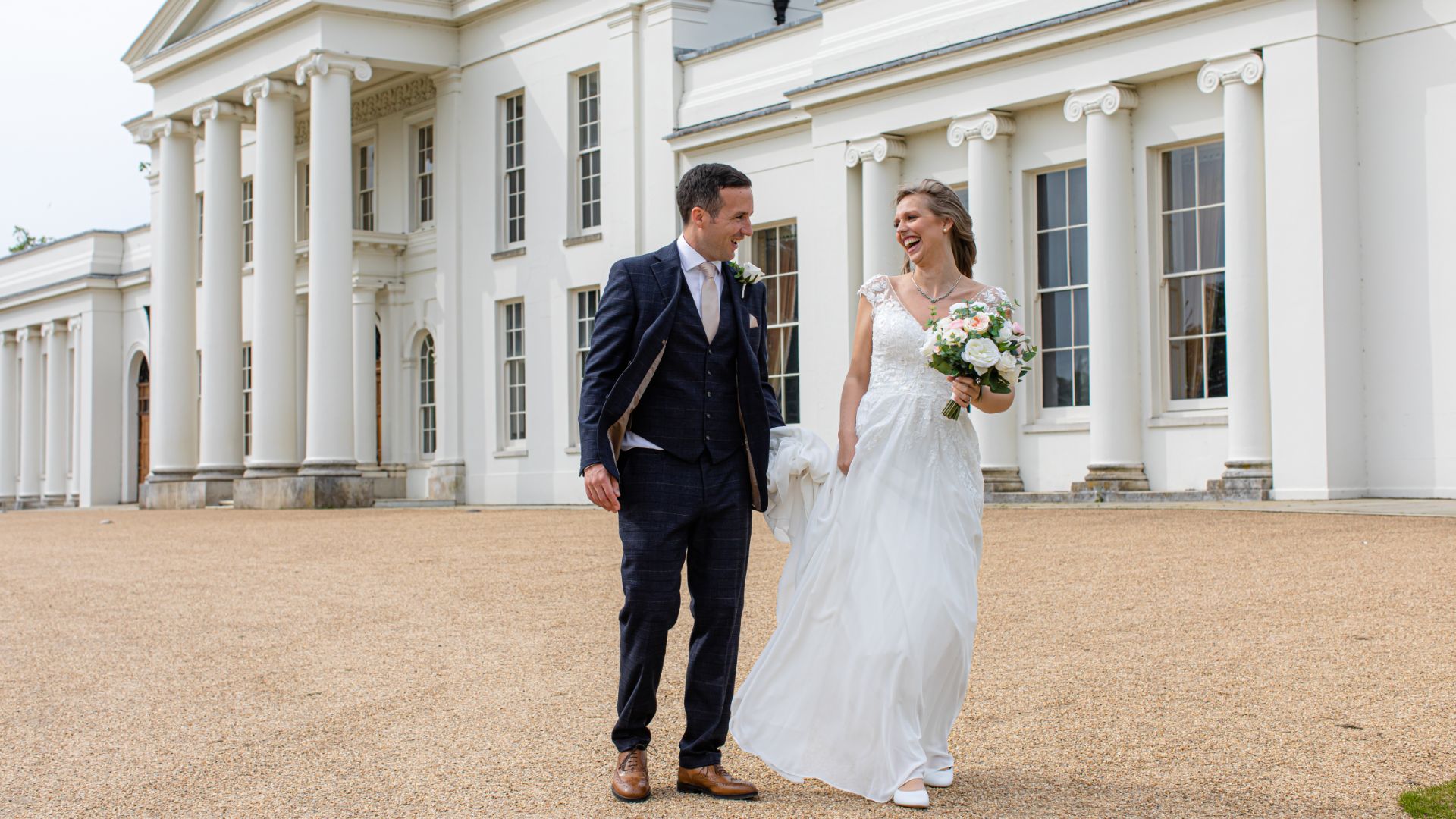 A bride smiling at her groom as they walk outside of Hylands House. 