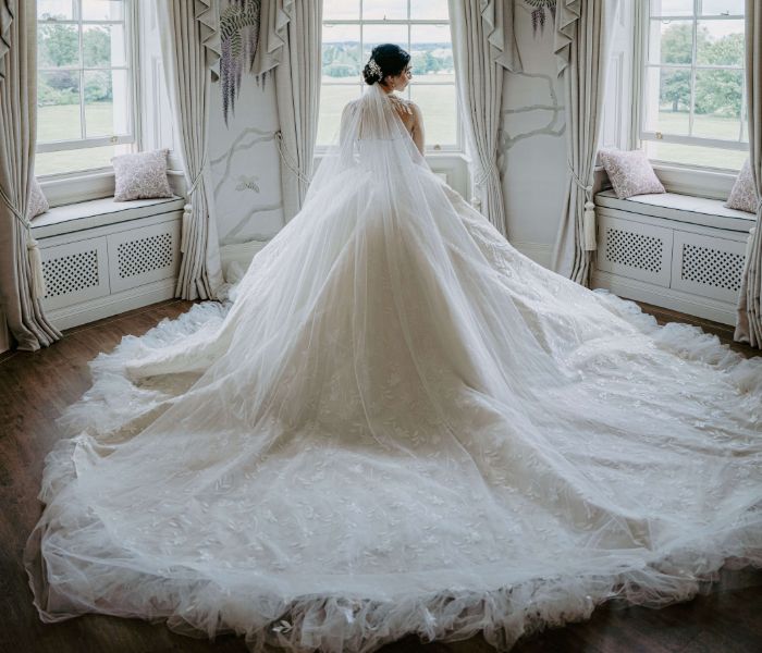 A bride wearing a long flowing white gown in the Wisteria Room looking over Hylands parkland. 