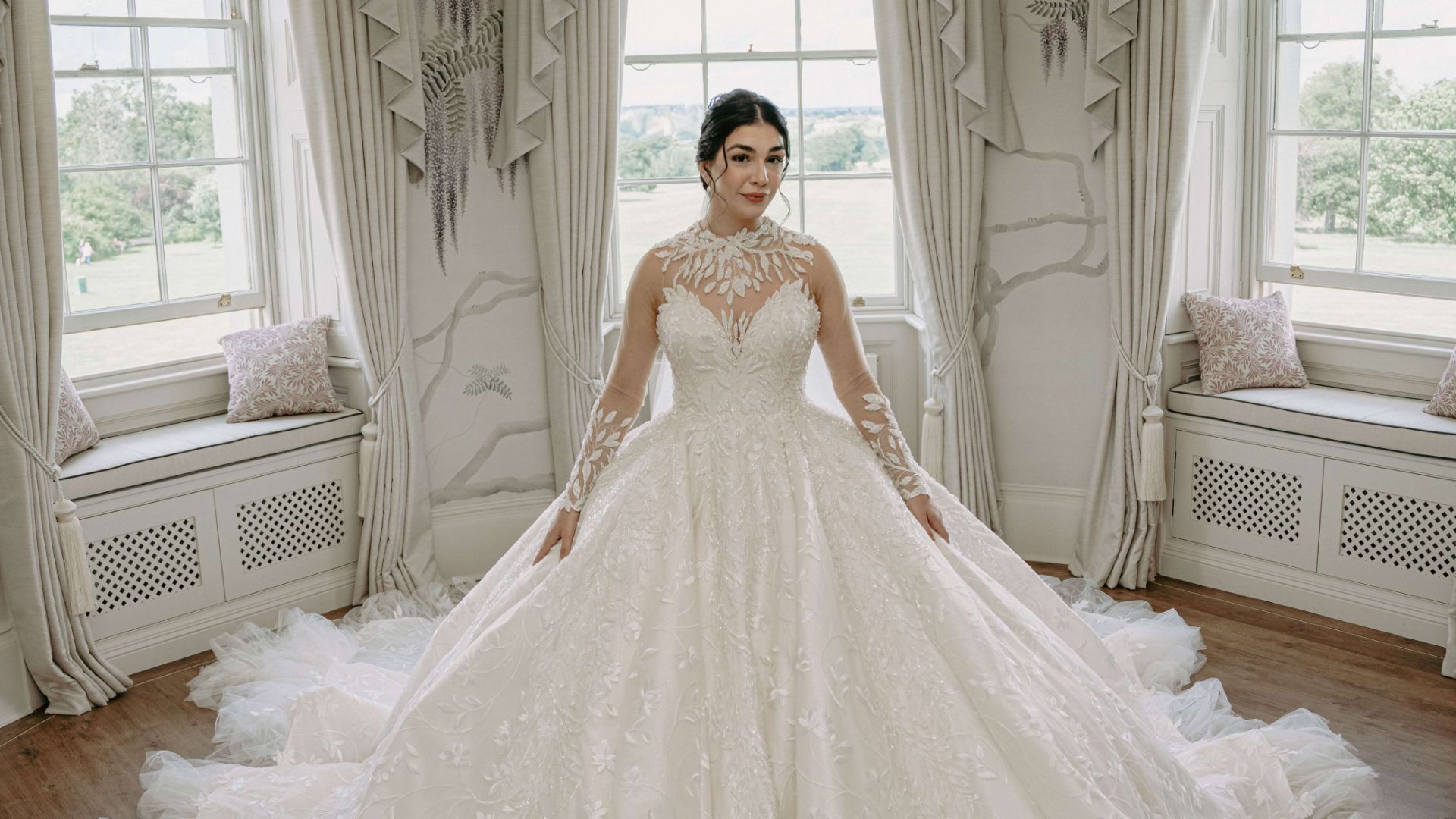 A bride wearing a long flowing white gown in the Wisteria Room looking over Hylands parkland. 