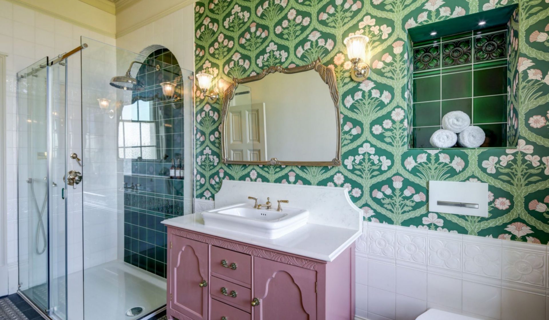 The bathroom of the Wedding Suite featuring a shower with dark green tile and a pink vanity.